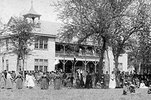 A large group outside the two-story school. Several stand in a circle holding hands.