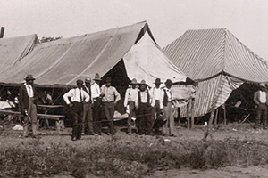 A group of men stand outside tents of various sizes.