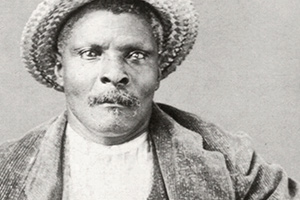 Portrait of Caesar Bowlegs wearing a straw hat, and a suit with a jacket and waistcoat.