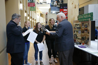 Judges ask three smiling students questions about their exhibit project.