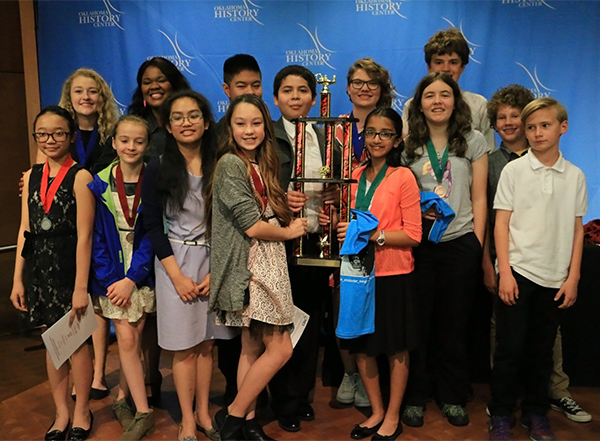 A group of young students pose with their medals and a large trophy