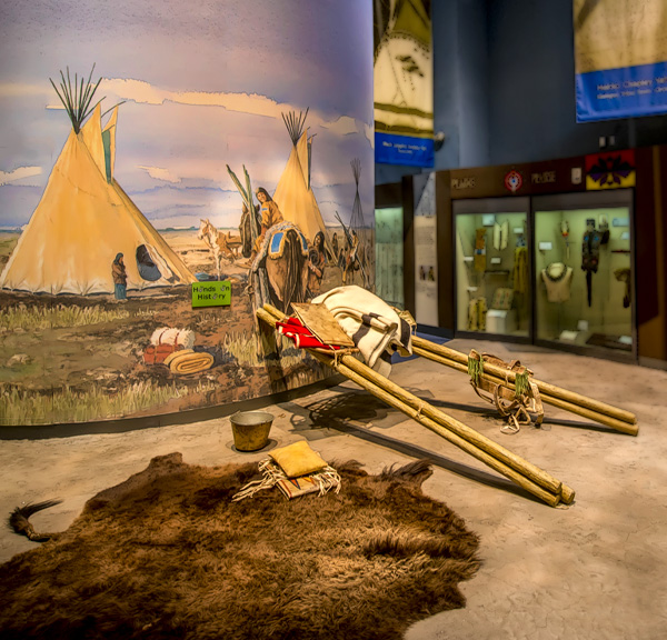 A travois in front of a wall with tipis painted on it.