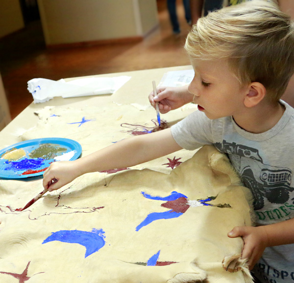 A young boy paints on a large piece of leather