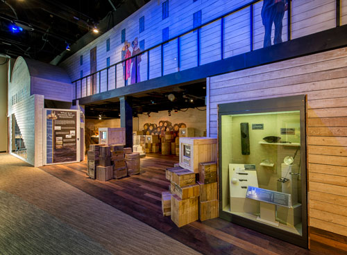 Part of the exhibit showing artifacts in a case and crates. The wall is made took look like a steamboat deck.