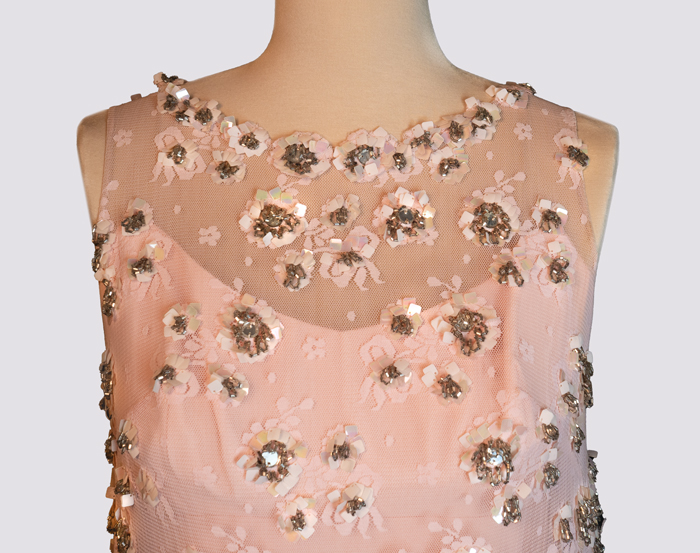 A light pink sleeveless dress with a sheer pink lace overlay decorated with pink sequins and gold and silver beads