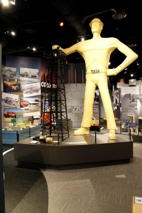 A model of the Golden Driller statue with a man resting his hand on top of an oil derrick