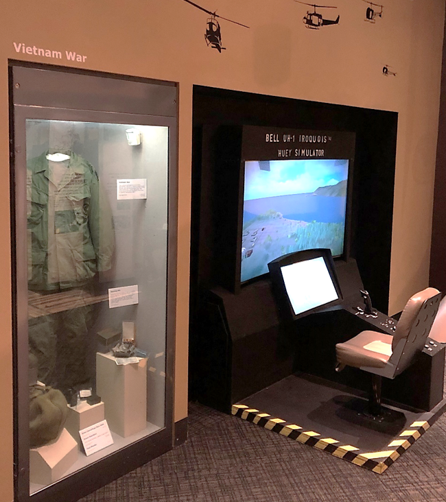A helicopter flight simulator game with a chair in front of a monitor and large screen