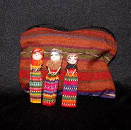 A woven bag and three small dolls resembling women with covered heads in long dresses.